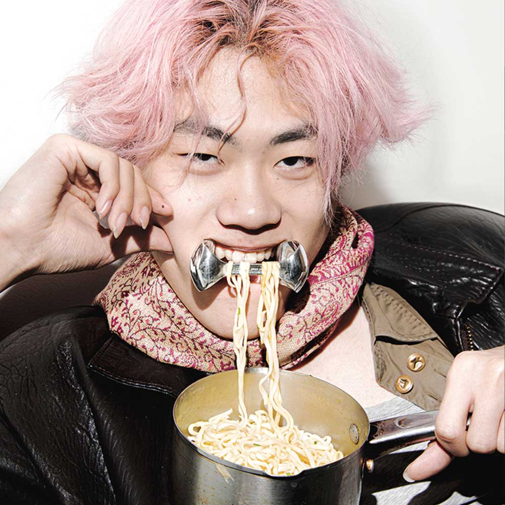 a man with pink hair is eating noodles